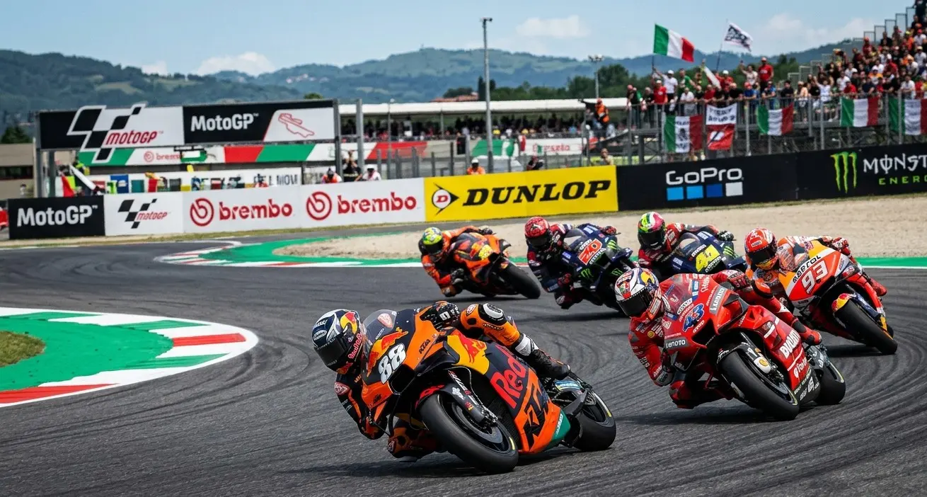 Piloti MotoGP in piega durante una gara del mondiale 2026, duello tra Ducati e KTM su circuito internazionale.