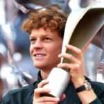 Jannik Sinner sorridente solleva un trofeo appena vinto.