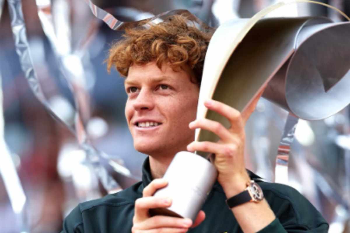 Jannik Sinner sorridente solleva un trofeo appena vinto.