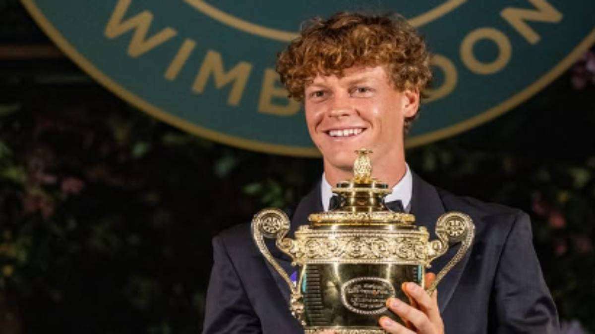 Jannik Sinner vestito elegante posa sorridente con la coppa del Torneo di Wimbledon 2026.